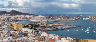 Las Palmas de Gran Canaria limanının yüksek açılı görüntüsü. Gemi gemileri konteynır vinçlerinin ve tersanelerin yakınına yanaşsın. Bir yat limanı yelkenlileri barındırır, şehir volkanik tepelere yayılır..