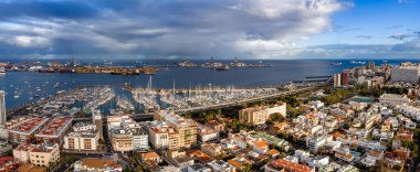 Las Palmas de Gran Canaria 'nın hava görüntüsünde marina yatları, Las Palmas Limanı vinçleri ve sondaj platformları, şehir blokları, kışın ışık kulesi ve kargo gemileri görülüyor..