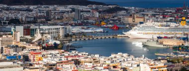 Las Palmas de Gran Canaria 'daki Puerto de la Luz' un yüksek açılı görüntüsü beyaz bir yolcu gemisi, endüstriyel rıhtımlar, römorkörler ve kış ışığında palmiye kaplı bir gezinti güvertesi gösteriyor..