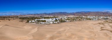 Hava görüntüsü, Gran Canaria 'daki Maspalomas Kumulları' nın beyaz tatil beldelerine ve palmiye ağaçlı sokaklara yuvarlandığını, volkanik dağların gün ortası ışığı ve kobalt gökyüzünün ötesinde olduğunu gösteriyor..
