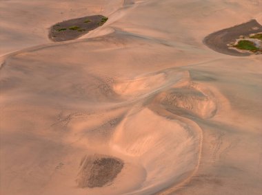 Gran Canaria 'daki Maspalomas Kumulları' nın hava görüntüsü rüzgar şeklindeki tepeler, oyuklar, seyrek yeşil alanlar, daha koyu düzlükler ve ılık gün ışığı altında soluk ayak izleri gösteriyor..