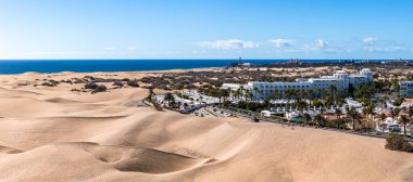 Gran Canaria 'daki Maspaloma Kumulları Atlantik' e kadar uzanıyor. Dalgalanan kum tepeleri, ufuktaki Maspalomas Deniz feneri, beyaz tatil köyü binaları, ve gün ortası aydınlığında palmiye kaplı sokaklar..