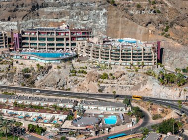 Gran Canaria 'da kavisli cepheleri ve balkonları olan teraslı otellerin gün ortası manzarası, yılansı sonsuz havuz, palmiye manzarası, sarı koç ve mavi havuzlar..