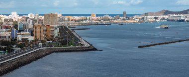 Las Palmas de Gran Canaria 'nın geniş kıyı manzarasında Avenida Maritima, Torre Woermann, limanda yolcu gemileri ve yumuşak gün ışığında hızlı sarı bir feribot görülüyor..