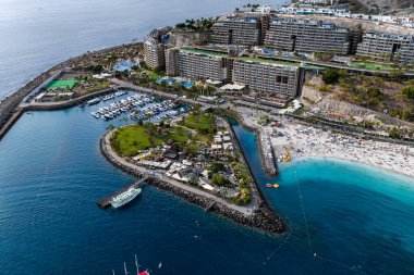 Anfi del Mar 'ın Gran Canaria' daki hava görüntüsü, yarımadadan yapılmış bir adam, küçük bir marinada beyaz yatlar, turkuaz bir göl, beyaz kum plajı ve yarı dairesel dalgakıranlar gösteriyor..