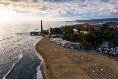 Gran Canaria 'daki Aerial Maspalomas Sahili sol tarafta deniz fenerini, kıvrımlı sahili, altın kum üzerinde güneşlenenleri, sakin Atlantik' i ve Meloneras 'a doğru tatil beldelerini gösteriyor..