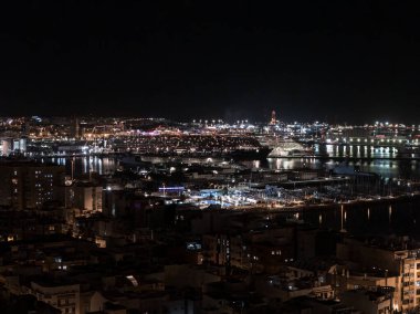 Las Palmas de Gran Canaria limanının gece görüşü, limana yanaşan yolcu gemileri, sakin limanı yansıtan ışıklar, direkli limanlar, şehir blokları, uzun pozlama görünümü ve kontrastlı limanlar..