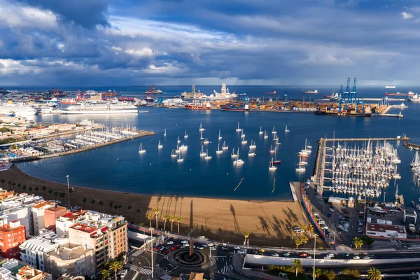 Las Palmas de Gran Canaria havadan kumlu sahil, marinalar ve yelkenlileri gösteriyor. Mavi turnalar ve yolcu gemileri öğleden sonra bulutların altında Puerto de la Luz 'da yükseliyor..