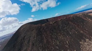 Hava aracı Fuerteventura 'daki siyah bir volkanik krater boyunca süpürüyor. Lav sırtlarını, toprak yolları, küçük yürüyüşçüleri, toprak ovaları, kumulları ve Atlantik' i gösteriyor.