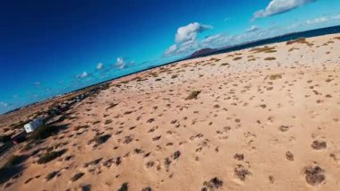 Fuerteventura 'daki Corralejo kum tepelerinin üzerindeki hava manzarası soluk kum, çalılık, araçlı bir sahil yolu, koyu volkanik bir koni ve uçurtma sörfçüleriyle Atlantik' i gösteriyor..