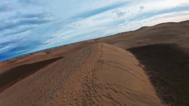 Gran Canaria 'daki Maspalom kumullarının üzerinden geçen hava aracı dalgalanmalar, rüzgar çizgileri, ayak izleri, küçük figürler ve katmanlı bulutların altında Atlantik ufkunun üzerinde süzülüyor..