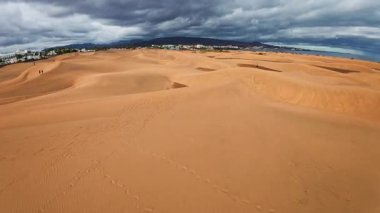 Hava kamerası Maspalomas 'ın tepelerini, Gran Canaria' daki tepeleri, ayak izlerini, insanları, tatil köylerini, palmiye ağaçlarını ve denizi dramatik fırtına bulutları altında tarıyor..