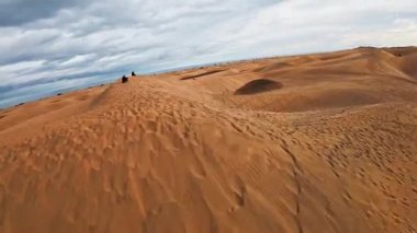 Hava görüntüsü Gran Canaria 'daki Maspalom kumullarını gösteriyor. Uzun dağ sırtları okyanusla birleşiyor. Kamera alçaktan hareket ediyor, dalgalanma ayrıntılarını gösteriyor, gölgeler, oyuklar, ziyaretçiler ve ayak izleri..