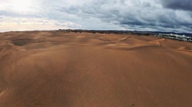 Gran Canaria 'daki Maspalomas kumullarının hava araçları altın kum tepeleri, beyaz tatil köyleri binaları, turistler, ayak izleri, fırtına bulutları ve süpürme kamera hareketleri gösteriyor..