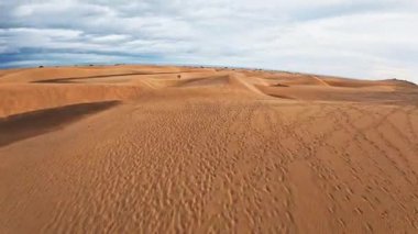 Gran Canaria 'daki Maspalomas kumulları üzerinde havada süzülüyor. Turuncu kahverengi çıkıntılar, ayak izleri, küçük ziyaretçiler ve Atlantik ufku yumuşak bulutlu gün ışığında görünür..