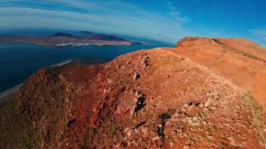 İHA görüntüsü, İspanya, Lanzarote 'deki Famara kayalıkları boyunca süpürüyor, plajlara, turkuaz boğaza, La Graciosa' ya, beyaz yerleşim yerine, dolambaçlı yola, sıcak güneş ışığına doğru eğiliyor..