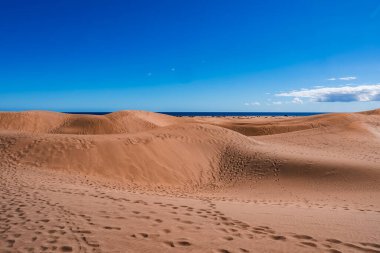 Dalgalanan altın kum tepecikleri Gran Canaria 'daki Atlantik Okyanusu' na doğru uzanır. Parlak gün ışığında dalgalı tepelerde ayak izleri ve güçlü kontrast....