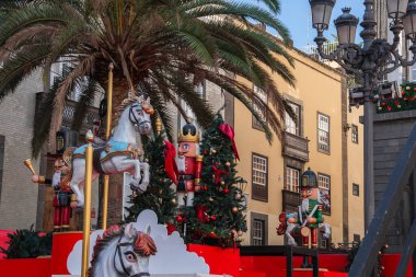 Büyük boy fındıklı krakerler ve atlı karınca atları Noel ağaçlarının ve Las Palmas, Gran Canaria 'da uzun bir palmiyenin yanında dururlar. Kanarya sarısı ve taş cepheleri şenlikli bir şehir meydanını çevreledi..