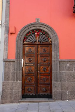 Las Palmas de Gran Canaria 'daki gri bir volkanik taş kemerde zengin oyulmuş ahşap çift kapılar bulunur. Yelpaze demiri ve kırmızı çelenkler bir tatil ziyareti öneriyor.