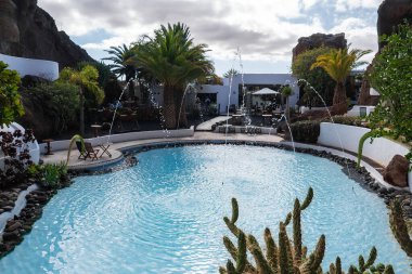 Lanzarote 'deki Lagomar Müzesi' nde kemerli su jetleri ve lav kaya duvarları ve palmiyelerin olduğu avlu. Beyazlaşmış formlar ve kafe masaları öğleden sonra vakti ortaya çıkar..