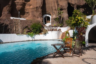 Beyazlatılmış duvarlar, mağara geçitleri ve Lanzarote, Nazaret 'teki Lagomar House' da avlu havuzu. Kaktüs ve su jetleri ahşap sandalyeleri kuşatır..