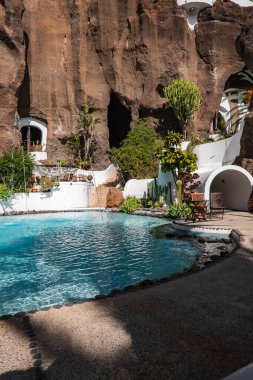 Lanzarote, Nazaret 'te volkanik kayalara karşı güneşli avlu havuzu. Beyazlaşmış kemerler ve tüneller, palmiyeler ve öforbi kaktüsü, su jetleri, öğle ışığı ve derin gölgeler..