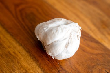 Tek bir sarımsak soğanı zengin bir ahşap yüzeyde bulunur. Ilık doğal ışık ve sığ alan derinliği kök tabanı ve karanfil hatlarını ortaya çıkarıyor..