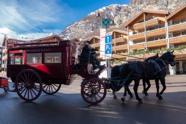 Resmi bir sürücü olarak Mont Cervin Sarayı at arabası Zermatt 'tan geçer. İki siyah ata yol gösterir. Tabelaları, dağ evini ve uzak Matterhorn' u geçer..