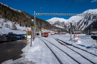 Karlı yollar Zermatt 'ta küçük bir istasyona çıkıyor. Kırmızı bir çarklı tren oturuyor. Tepedeki hatlar, sinyal direkleri ve park halindeki araçlar gün ortasında tırabzanlara ulaşabildiklerini gösteriyor..