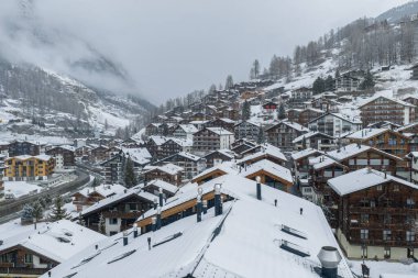 İsviçre 'nin Zermatt kentinin karlı hava manzarası, kadife tabakalarını, modern locaları, dolambaçlı yolları ve bulutlu zirvelerin altındaki kompakt yerleşimi gösteriyor..
