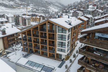 Hava sahnesi İsviçre 'nin Zermatt kentindeki modern bir alp oteli gösteriyor. Yüksek çatılı, cam cepheli ve karlı bir yamaçtaki ahşap kiremitler arasında ahşap çerçeveli..