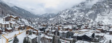 İsviçre 'nin Zermatt kentinin havadan görünüşü, kilise kulesi, dağ evleri, oteller, kayak pistleri ve sarmal yollar, dik orman yamaçlarıyla çevrili..
