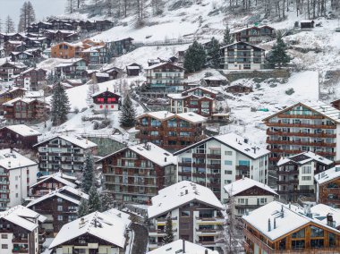 İsviçre, Zermatt 'ta kar battaniyeleri, karaçam ve çam ağaçları, kırmızı kepenkli bir dağ evi, eğimli çatılar ve yumuşak ışıklı yoğun teraslı binalar..