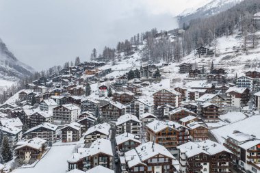 İsviçre 'nin Zermatt kentinin havadan görünüşü, taze kar, dolambaçlı sokaklar, kırmızı bir dağ evi, tarla ormanı ve Matterhorn yakınlarında sessiz bulutlu bir ışık.