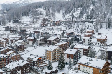 İsviçre 'nin Zermatt kentinin hava görüntüsünde taze kar, köknar ağaçları, teraslı yamaçlar, kayak pistleri, sessiz ışık ve katmanlı yamaçlar altında bulunan dağ evleri görülüyor..