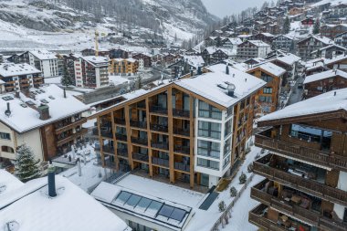 İsviçre 'nin Zermatt kentinin karlı hava manzarası, klasik tebeşirler arasında kereste balkonları ve cam cepheli, yumuşak ışık ve düşen karla dolu modern bir alp oteli gösteriyor..