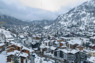 Zermatt, İsviçre 'nin hava manzarası, karlı Chalet' ler, kilise kulesi, dolambaçlı sokaklar ve kışın Alp tepelerinin altındaki dar bir vadi..