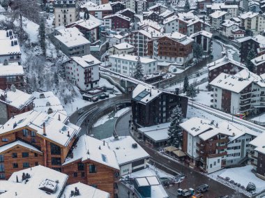 İsviçre, Zermatt Havalimanı kıvrımlı nehir ve yollar, elektrik taksileri ve yumuşak kış ışığı ve kar yağışı altında dar bir demiryolu üzerindeki dağ evleri ve otelleri gösteriyor..