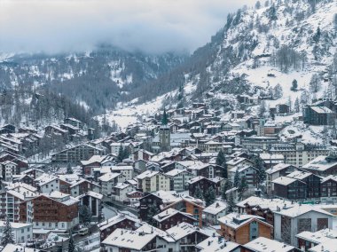 Zermatt, İsviçre 'nin hava manzarası, karlı, kümelenmiş dağ evleri, oteller ve yeşil spiral kilise saat kulesi, dolambaçlı sokaklar, yumuşak kış ışığı ve alçak bulutlar..