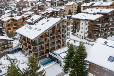 Zermatt, İsviçre 'nin havadan görünüşü, tebeşir, kereste ve cam otel, derin balkonlar, kısmi açık havuz, arabasız sokaklar ve yumuşak bulutlu ışık..