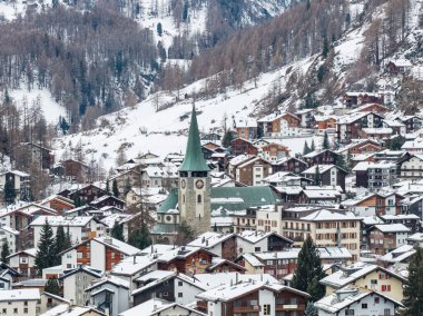 Zermatt, İsviçre, yeşil çatılı ve saat kulesiyle St. Mauritius Kilisesi 'ni gösteriyor, karla kaplı kireçler, tarla kuşları ve kayak yapmak için soğuk bir mevsim..
