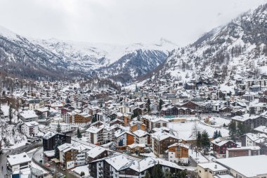 Zermatt, İsviçre 'nin havadan görünüşü, taze kar, Zermatt kilise kulesi, dağ evi otelleri, dolambaçlı sokaklar, donmuş spor sahası ve sessiz ışık altında Matterhorn..