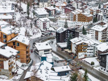 Zermatt, İsviçre 'nin hava manzarası, Chalets, localar, kıvrımlı sokaklar ve dar bir nehir gösteriyor. Kereste cepheleri ve balkonlar yumuşak bulutlu ışıkta taze karın altında otururlar..