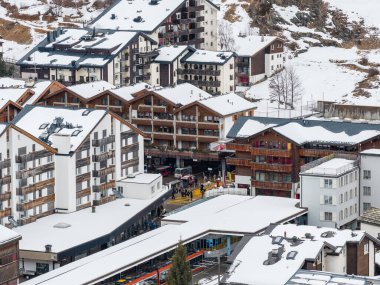 Merkez Zermatt, İsviçre 'nin havadan görünüşü, insanlar aşağıdaki yaya geçitlerinde ve platformlarda yürürken, dağ evlerinin çatılarında kar ve tren istasyonu yakınlarındaki kereste balkonları..