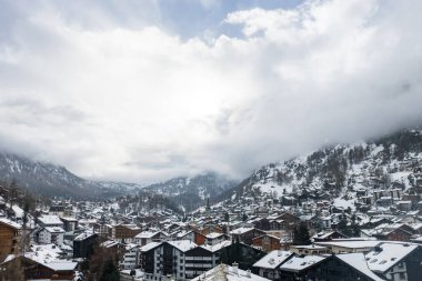 Kar yağdıktan sonra İsviçre, Zermatt 'ın hava görüntüsü. Chalet 'ler ve oteller vadi yamaçlarında. Yeşil kilise kulesi bulutların sürüklenmesi ve Matterhorn 'un saklanması için merkezde duruyor..