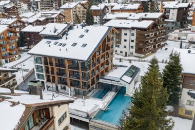 Hava sahnesi İsviçre 'nin Zermatt şehrinde dumanı tüten bir açık havuzu ve kaplıcası olan lüks bir alp oteli gösteriyor. Kar, ahşap ve cam tasarımı, kiremitler, yumuşak bulutlu ışık..