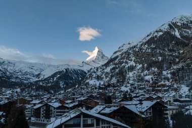 İsviçre, Zermatt 'ın panoramik kış manzarası. Matterhorn dağ evi çatıları ve otellerin üzerinde ilk ışığa yakalanırken, engebeli yamaçlar ve soğuk mevsimde şafak vakti yumuşak bir bulut..