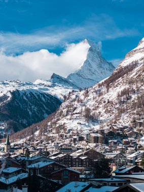 Zermatt, İsviçre Matterhorn 'un altında bir bulut gibi duruyor. Chalet 'ler ve oteller yokuşu tırmanır, kilise yükselir, gün ortası ışığı ve derin mavi gökyüzü.