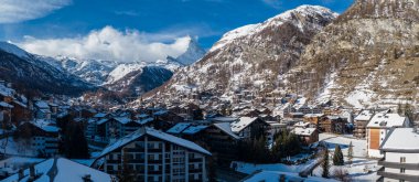 Zermatt, İsviçre, sunar dağ evleri çatıları, Zermatt kilise kulesi, ve Matterhorn. Gün ortası ışığı, geniş manzaralı güneşli yamaçları ve gölgeli çatıları tanımlar..