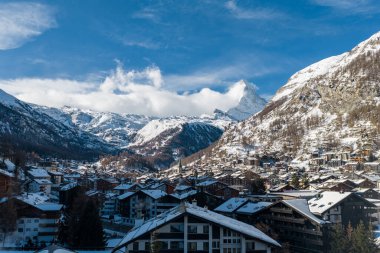 İsviçre 'nin Zermatt kentinin havadan görünüşü, tebeşir ve otellerde karla kaplı, kilise merkezi, bulutlarla yükselen Matterhorn, açık gökyüzü altında..